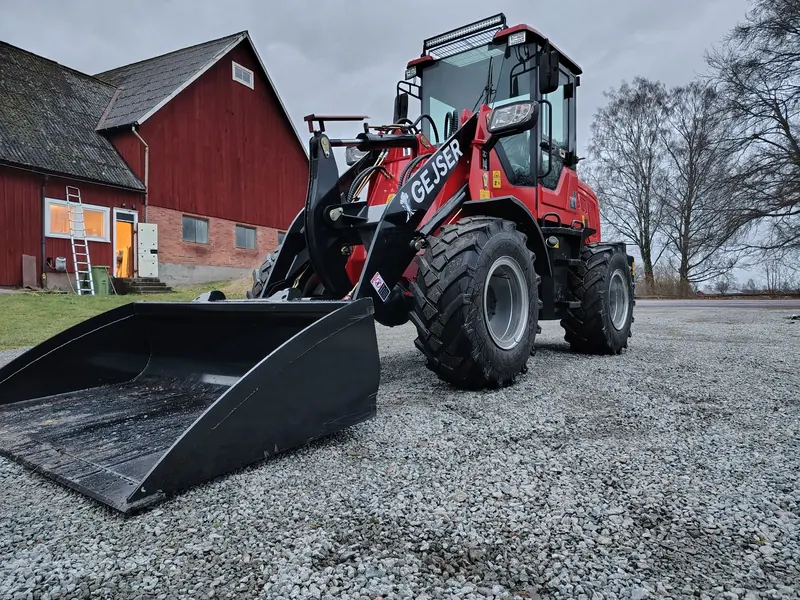 Gejser L20 hjullastare med hytt och planerskopa framför en röd lada