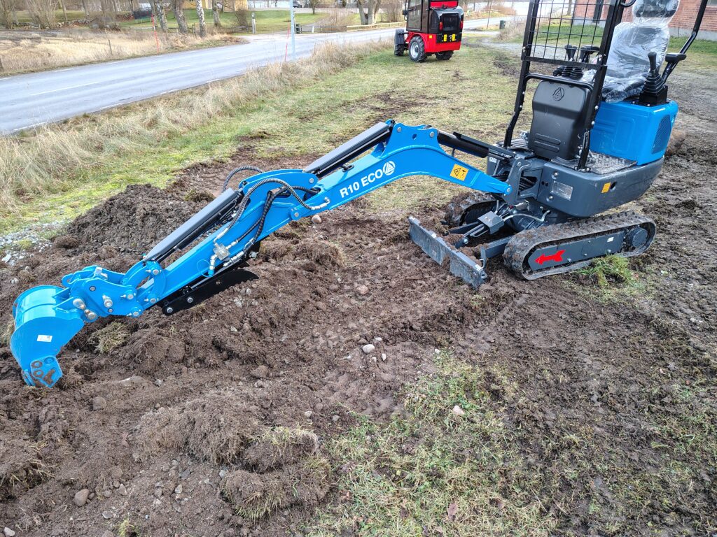 Blå minigrävare med lång grävarm och larvband vid markarbete.