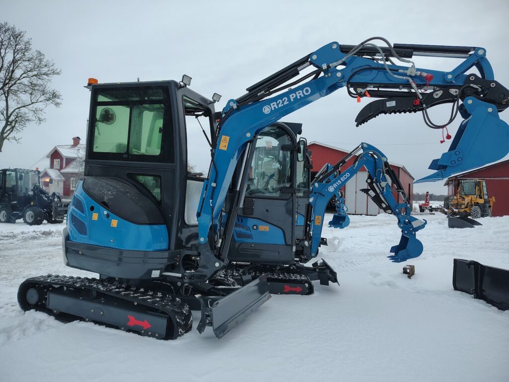 Blå minigrävare med larvband och skopa, redo för grävning och markarbete i vintermiljö.
