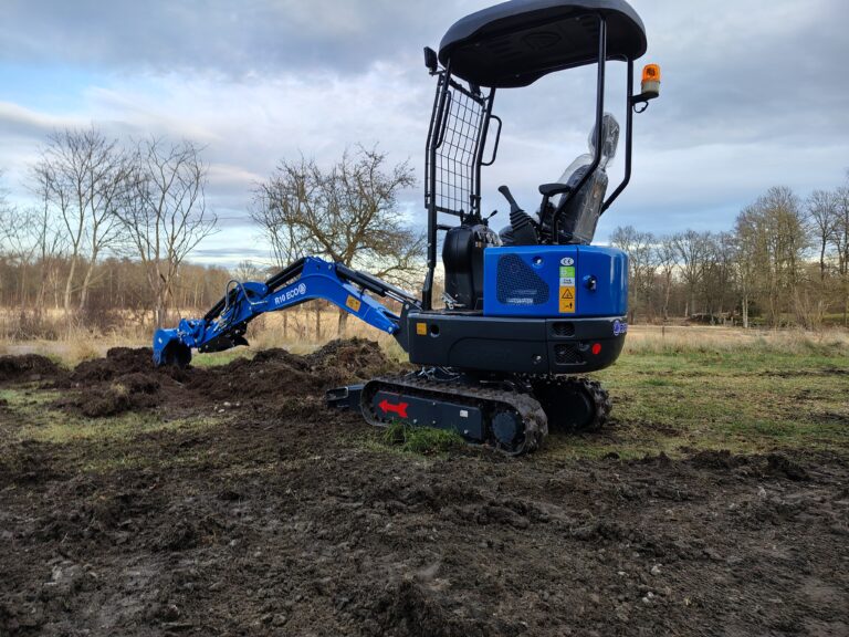 Blå minigrävare som gräver i marken med larvband och skopa.